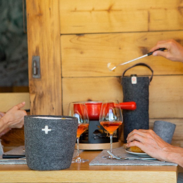 Baabuk Swiss red felted wool table mat on a wooden dining table with wine glasses and fondue set