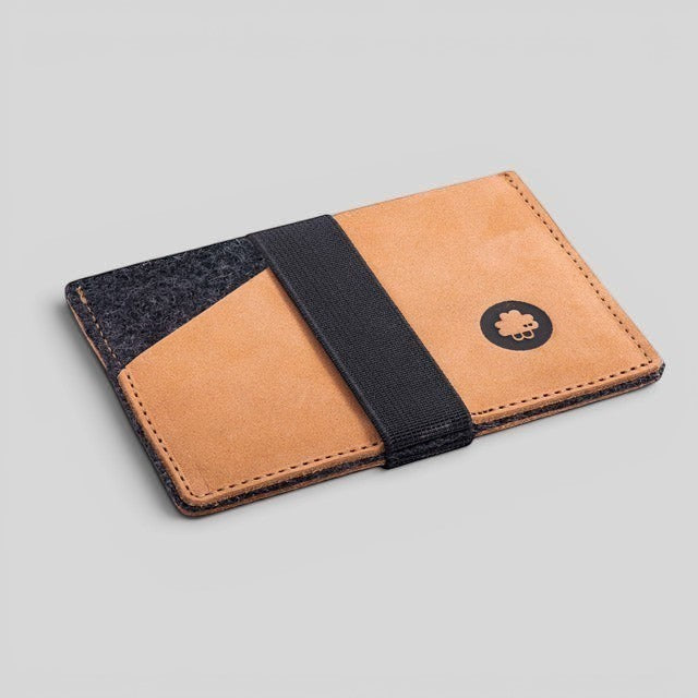Baabuk slim wallet in tan leather and grey wool with a black elastic strap and logo detail on a light background.