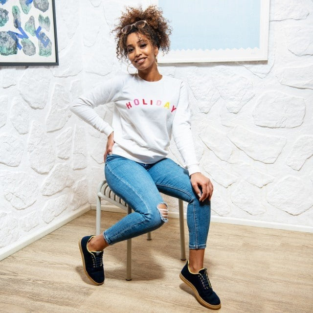 Baabuk Urban Wooler navy wool sneakers with yellow trim worn by a woman sitting on a chair in a bright room.