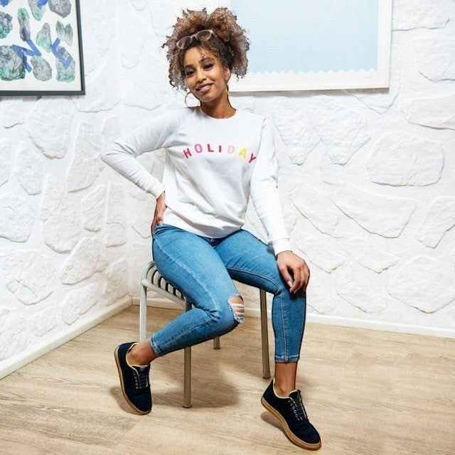 Baabuk Urban Wooler navy wool sneakers with yellow trim worn by a woman sitting on a chair in a bright room.