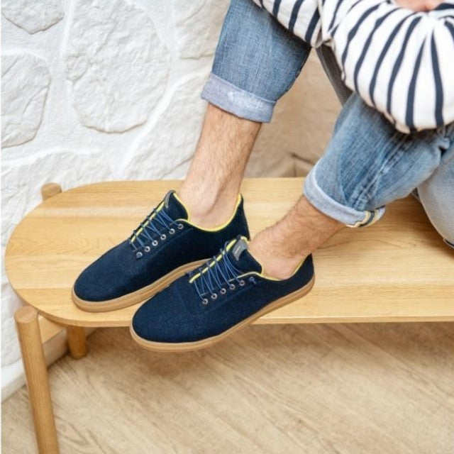 Baabuk Urban Wooler navy blue wool sneakers with yellow trim and elastic laces worn by a man on a wooden bench