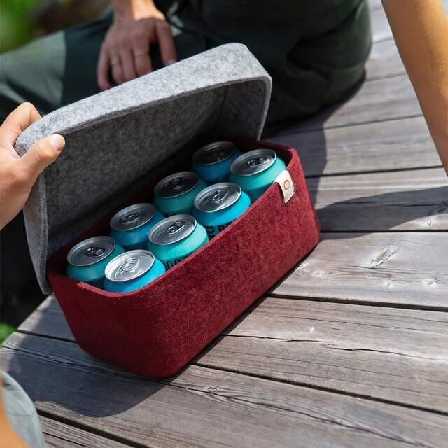 Baabuk bordeaux red wool beer cooler with grey lid, holding 8 blue beer cans on a wooden deck.