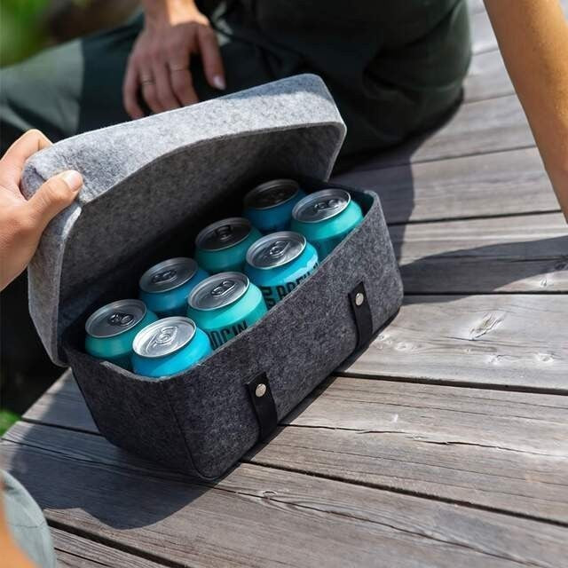 Baabuk dark grey wool beer cooler filled with 8 blue beer cans on a wooden surface.