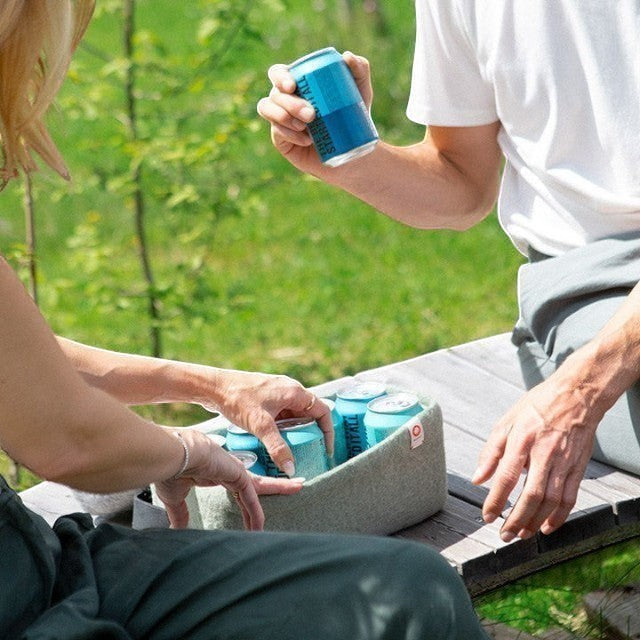 Baabuk light blue wool beer cooler holding cans on a wooden bench outdoors. Natural wool, handmade.