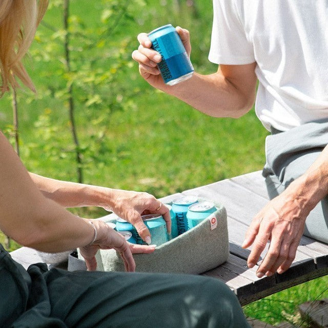 Baabuk light blue wool beer cooler holding cans on a wooden bench outdoors. Natural wool, handmade.