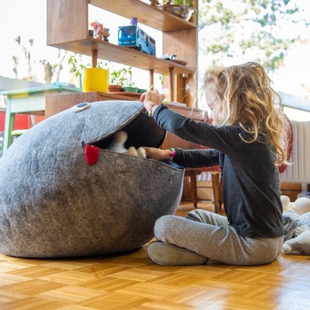 Child playing with a grey handmade Baabuk wool frog storage basket in a cozy nursery room.