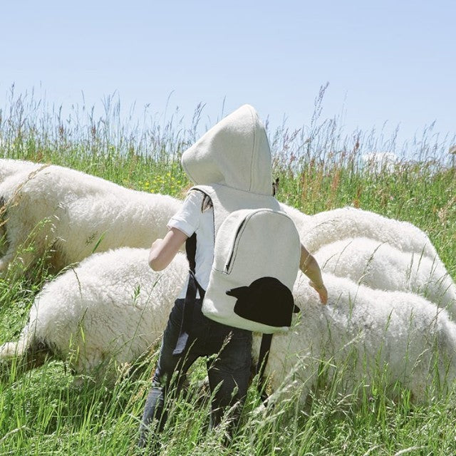 Child wearing a Baabuk wool hooded backpack in a field with Valais Blacknose sheep