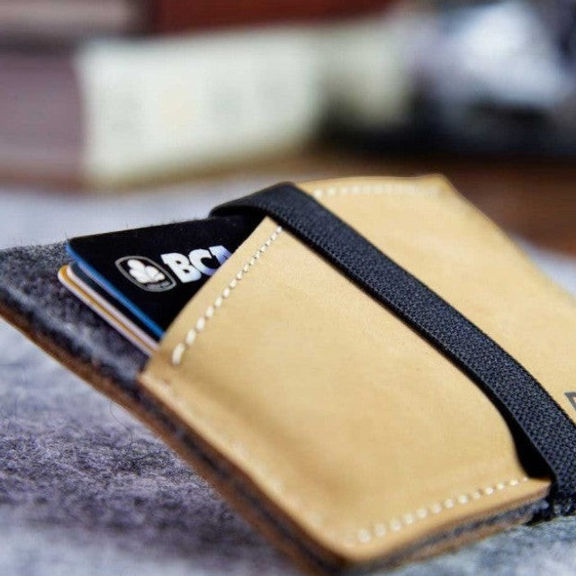 Baabuk slim wallet made of grey wool and tan leather with a secure black elastic strap holding credit cards.