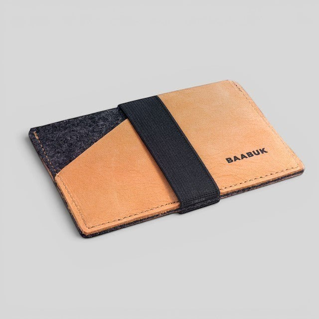 Baabuk slim wallet made of grey wool and tan leather with a black elastic strap for secure card storage.
