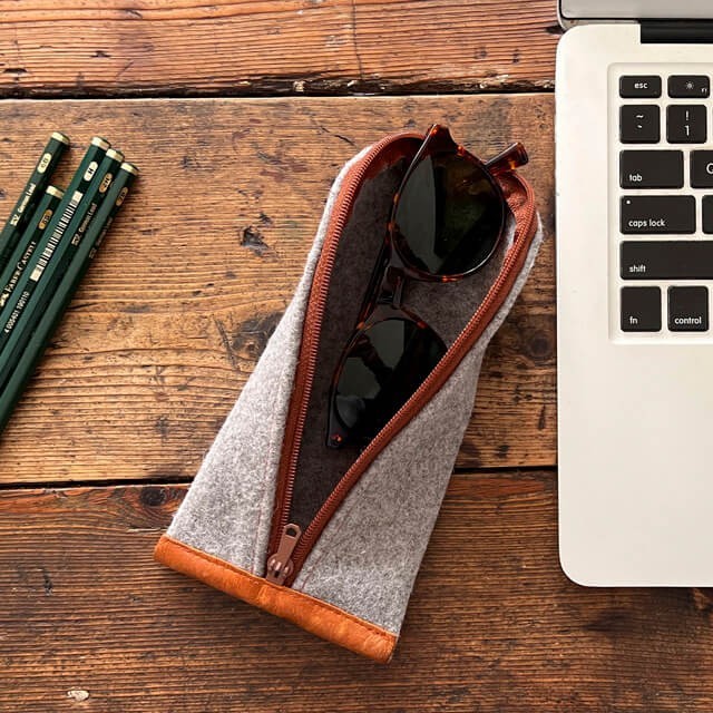 Baabuk grey wool pencil case with leather trim, holding sunglasses. Zippered pouch for pencils, glasses, or accessories.