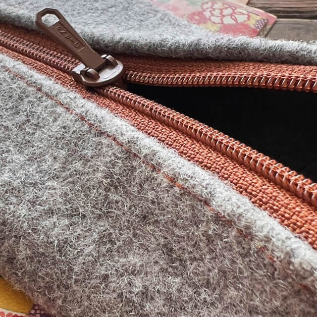 Baabuk grey wool pencil case with leather accents and a brown zipper closure. Measures 20cm x 10cm.