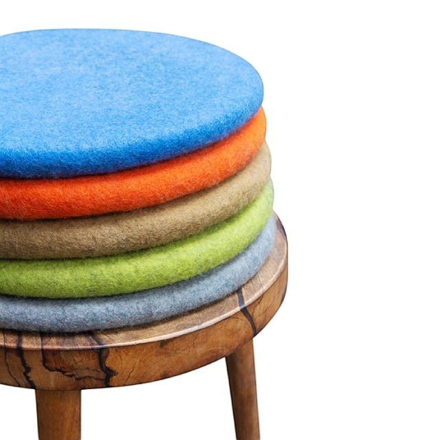 Stack of colorful handmade Baabuk wool sitting mats on a wooden stool, crafted from natural New Zealand wool.