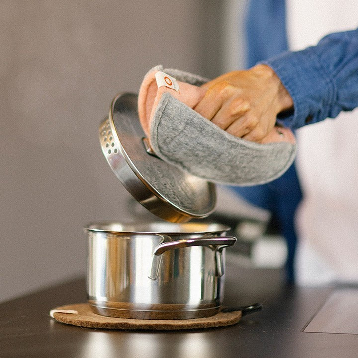 Baabuk brown felted wool trivet under a stainless steel pot on a kitchen counter with a matching pot holder