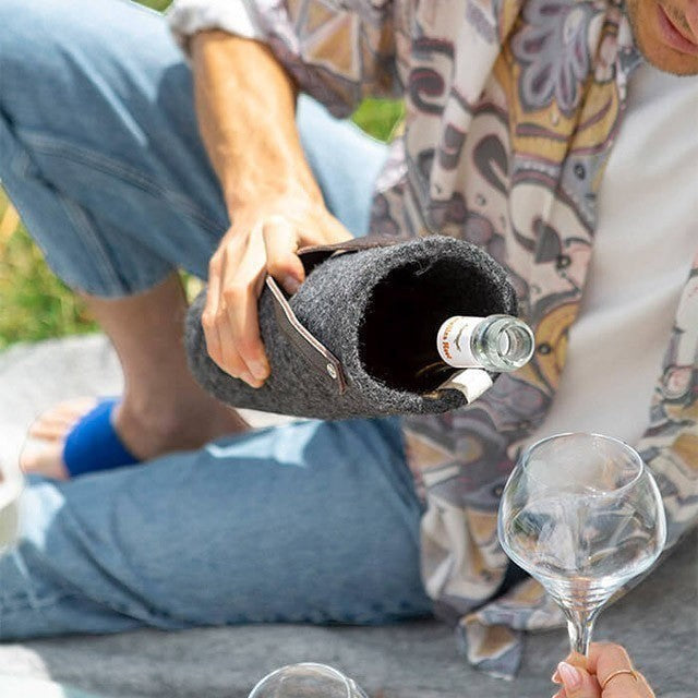 Baabuk dark grey wool wine cooler with leather strap, keeping a wine bottle chilled for outdoor enjoyment.