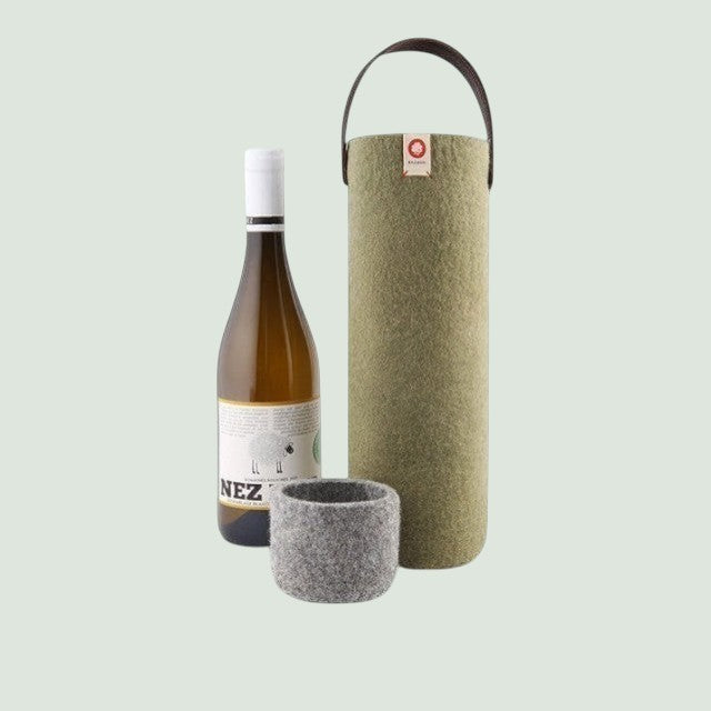 Un seau à vin en laine khaki de la marque Baabuk, muni d'une poignée en cuir, posé à côté d'une bouteille de vin blanc et d'un dessous de verre grey .