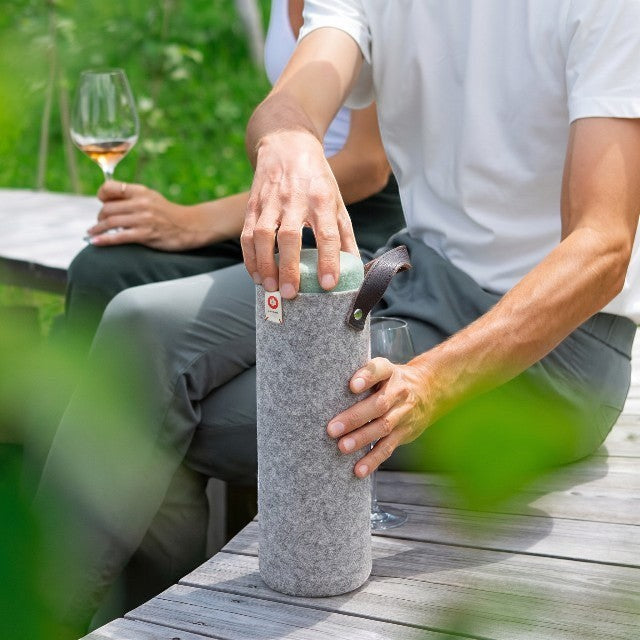 Baabuk light grey wool wine cooler with leather strap, keeping wine chilled outdoors.