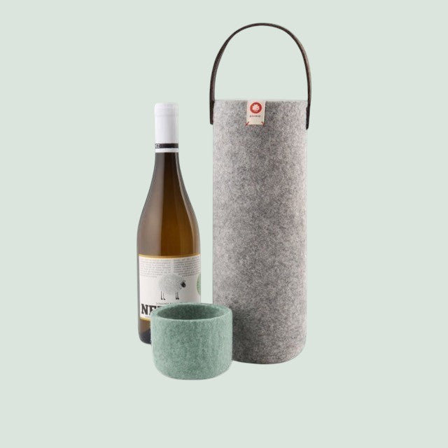 Baabuk light grey wool wine cooler with leather handle, next to a bottle of white wine and a green wool coaster.