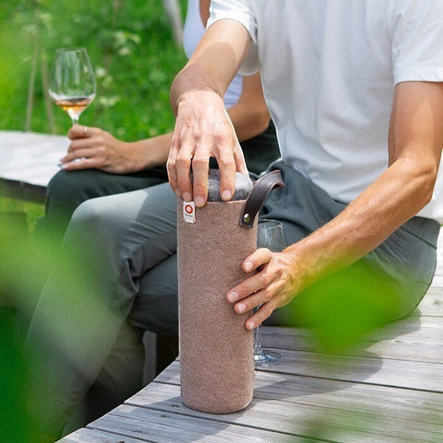 Baabuk Moka wool wine cooler with leather strap, keeping a wine bottle chilled outdoors.
