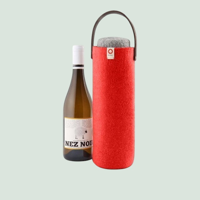 Un seau à vin en laine rouge « Baabuk Swiss » muni d'une poignée en cuir, à côté d'une bouteille de vin blanc.