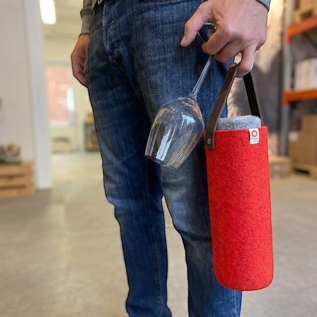 Baabuk red wool wine cooler with leather strap held by a person carrying a wine glass in a warehouse setting.