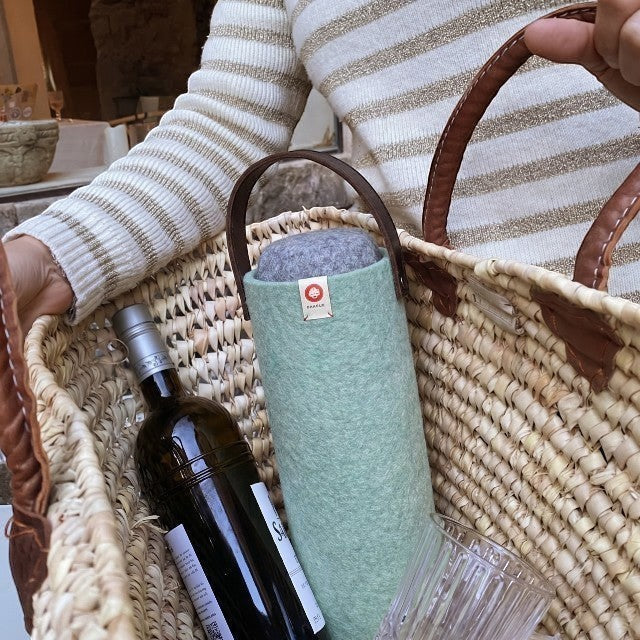 Baabuk turquoise wool wine cooler with leather handle, holding a wine bottle in a straw basket.