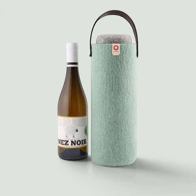 Baabuk turquoise wool wine cooler with leather handle next to a bottle of white wine.